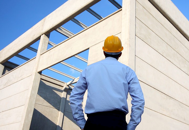 Businessman in hard hat peering up at building or warehouse under construction